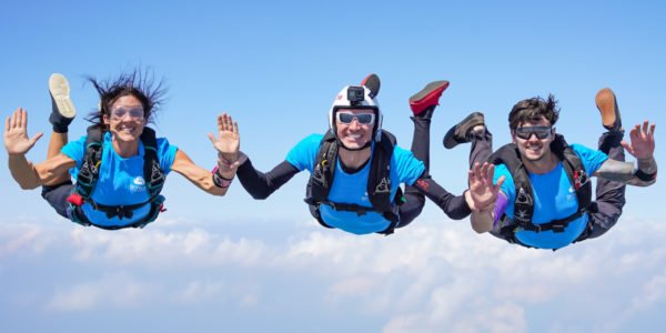 three skydivers hold hands in freefall and smile for the camera