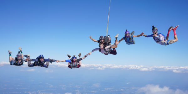 tandem skydiver holds hand with other skydivers in freefall