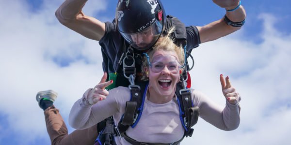 tandem skydiving student smiles and gives rock on symbol with hands