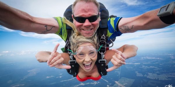 tandem skydivers in freefall smile at the camera