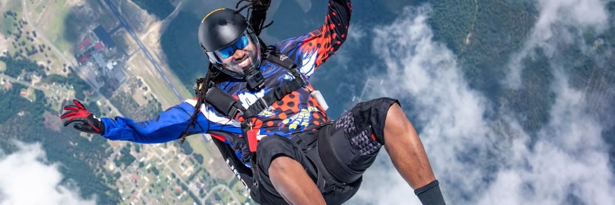 African American skydiver enters into freefall on his back and smiles for the camera