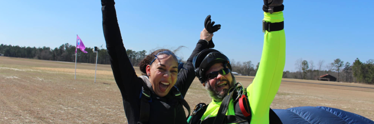 tandem skydivers land and smile with their arms in the air triumphantly