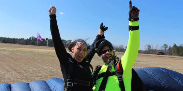 tandem skydivers land and smile with their arms in the air triumphantly
