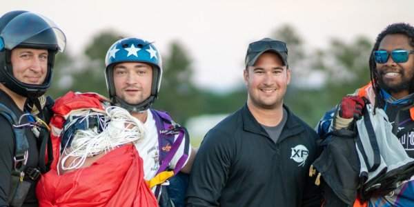 experienced skydivers and a student skydiver smile on the ground after landing their parachutes