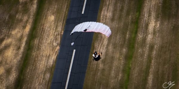 Ariel shot of skydiver going in for a swoop landing under a white parachute
