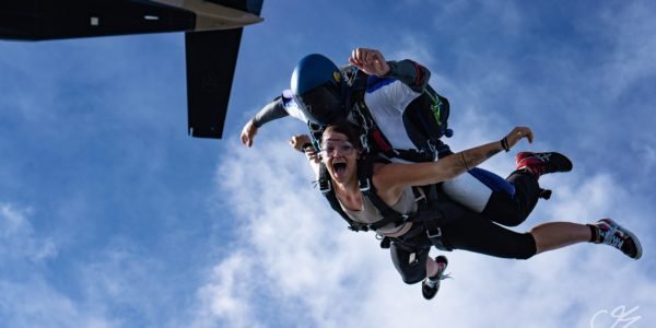 tandem skydivers enter into freefall and the female tandem student is smiling with her mouth open